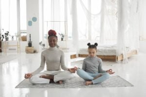 adorable african american kid with young mom practicing yoga in lotus pose