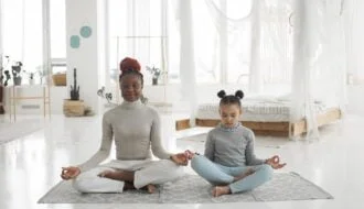 adorable african american kid with young mom practicing yoga in lotus pose