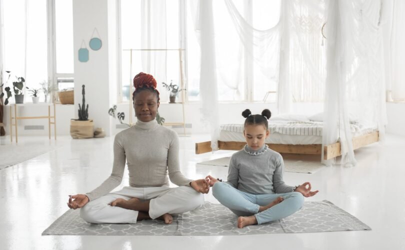 adorable african american kid with young mom practicing yoga in lotus pose